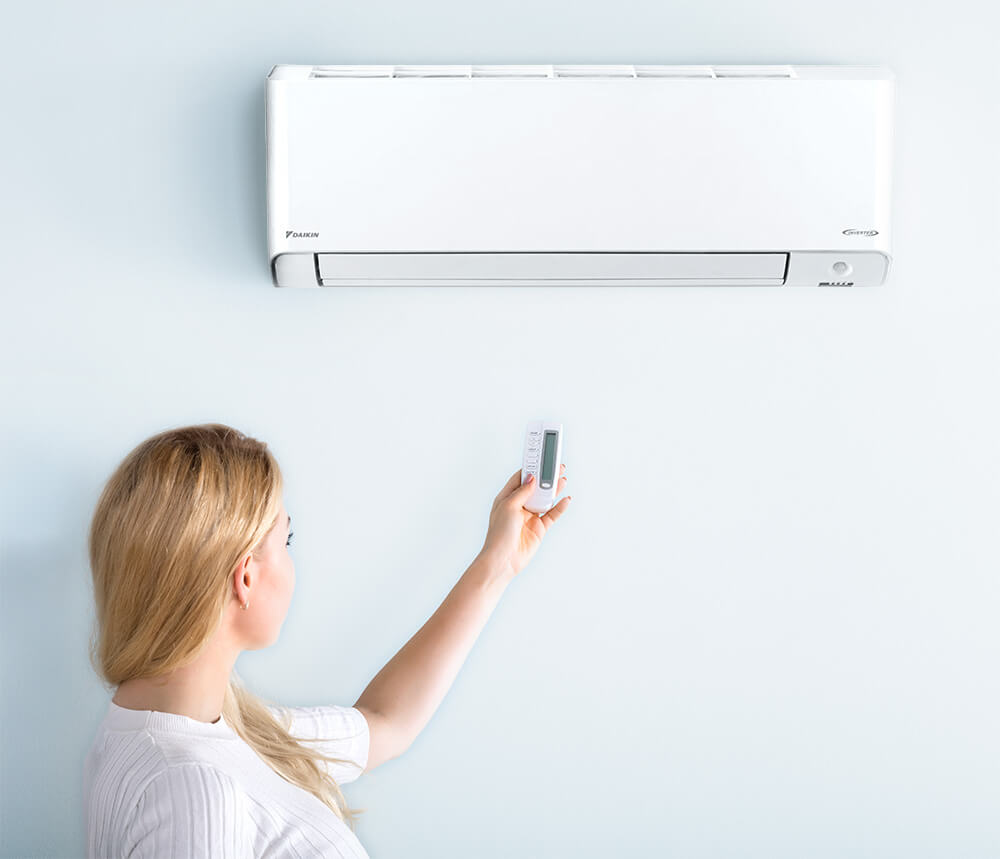 Image showing woman using air conditioning remote on Split System Reverse Cycle unit in modern Gold Coast home.