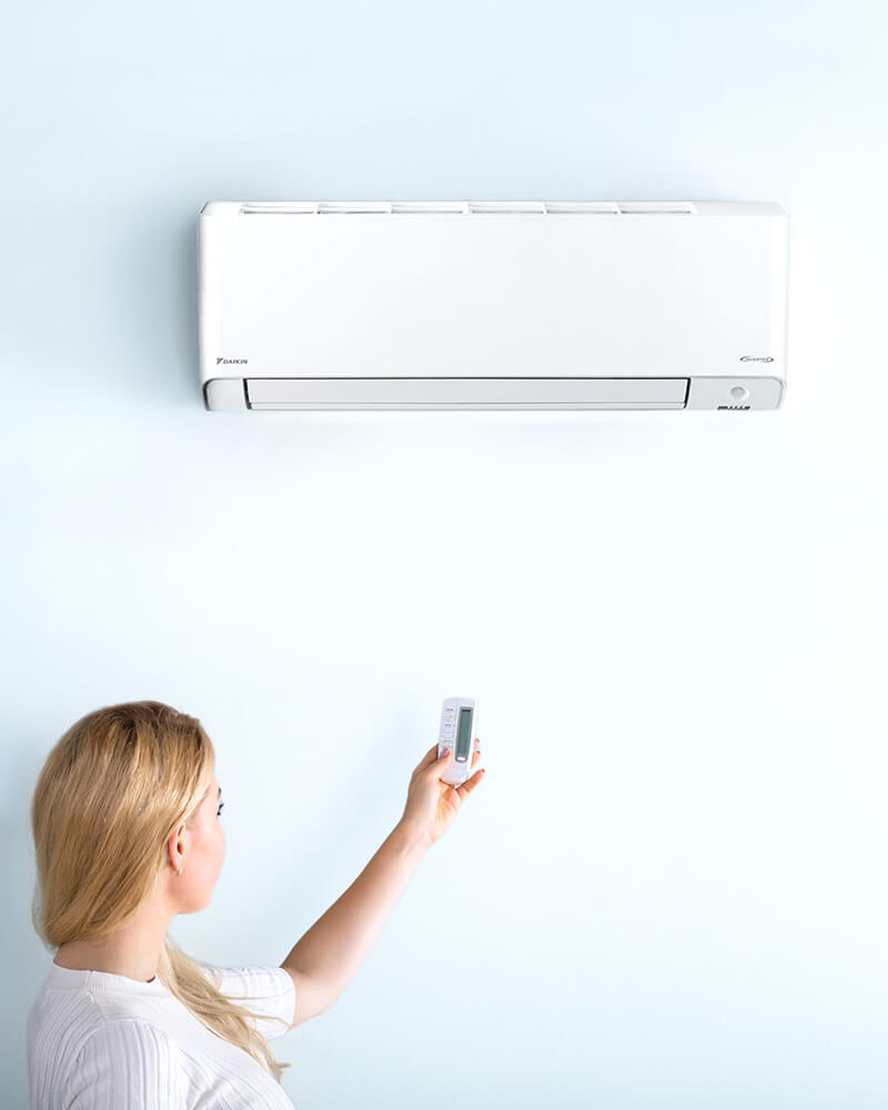 Image showing woman using air conditioning remote on Split System Reverse Cycle unit in modern Gold Coast home.